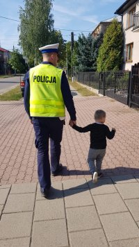 policjant ruchu drogowego prowadzi chłopca za rękę