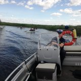 zdjęcie przedstawia funkcjonariusza na łodzi motorowej, w tle widoczna grupa kajakarzy