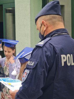 policjant trzyma dyplomy, w tle dzieci