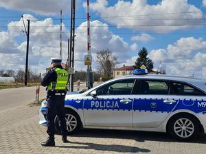 policjant ruchu drogowego stoi obok radiowozu w rejonie przejazdu kolejowego podczas działań &quot;bezpieczny przejazd&quot;