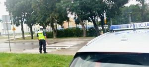 policjant ruchu drogowego w rejonie przejścia dla pieszych, po prawej stronie zdjęcia widoczny radiowóz