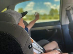dziecko w samochodzie, siedząc w foteliku wyciąga rączkę w kierunku okna