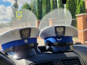 czapki ruchu drogowego na desce rozdzielczej radiowozu, w tle znaki drogowe informujące o przejściu dla pieszych