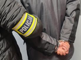 na zdjęciu policjant z zatrzymanym sprawcą kradzieży z włamaniem. Policjant trzyma zatrzymanego, który ma założone kajdanki na ręce trzymane z tyłu