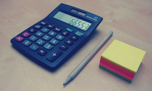 na biurku leżą kalkulator, długopis i karteczki samoprzylepne