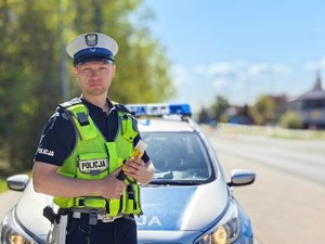 na fotografii policjant ruchu drogowego na tle radiowozu