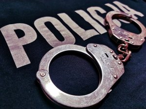 na granatowym tle z białym napisem POLICJA leżą kajdanki