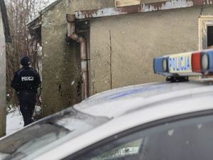 Na zdjęciu znajduje się dwóch funkcjonariuszy policji, radiowóz oraz budynek
