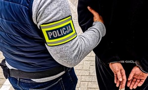 policjant i mężczyzna w kajdankach, obydwaj tyłem, widoczne dłonie w kajdankach